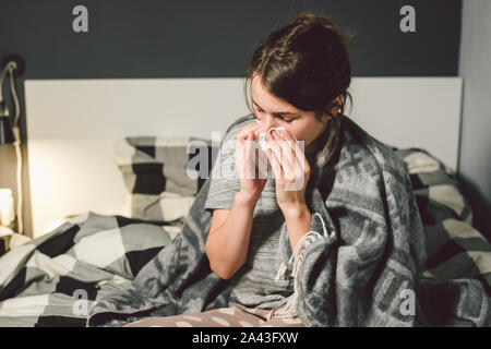 Malata con naso che cola, seduta in letto. donna senso di malessere e starnutire camera da letto. La donna il trattenimento del tessuto ,i sintomi di influenza. Healthcare Medical concept Foto Stock