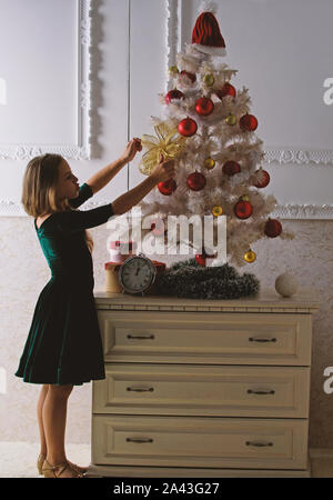 Ottenere incredibilmente entusiasti di natale. Kid ragazza nei pressi di albero di natale in attesa della mezzanotte orologio. Ultimi preparativi. Bambino festeggiano il Natale a casa. Giorno preferito dell'anno. Celebrazione della Messa di Natale. Foto Stock