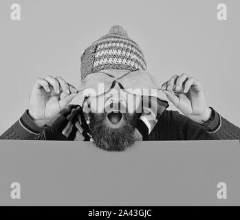 Ragazzo con sorpresa di fronte indossa caldo hat su sfondo rosa, copia dello spazio. Uomo con la barba si chiude gli occhi con cherry tree foglie. Autunno e caduta foglie concetto. Stagione Autunnale e hipster style Foto Stock