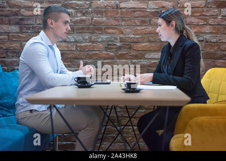 Due giovani di sesso maschile e di sesso femminile aziendale multirazziale persone che lavorano collegati con dispositivi tecnologici al bar. Due giovani colleghi creative lavorando wi Foto Stock