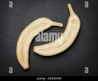 Tagliato a metà banana scuro sulla lastra di pietra. Foto Stock