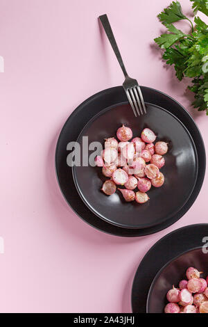 Bella ravanelli arrosto in una piastra nera sul tavolo rosa vicino. Foto Stock