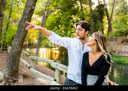 Un uomo di punta il dito lateralmente mentre abbraccia la sua ragazza che guarda a lui nell'amore. Foto Stock