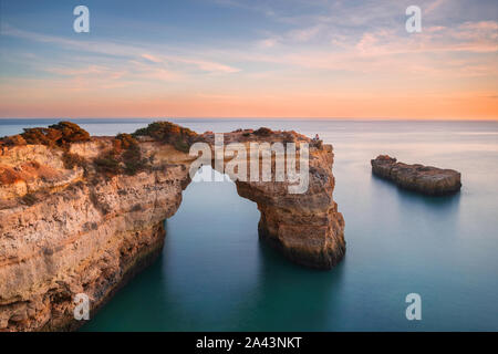 Spiaggia di Algarve, coppia romantica e guardare il tramonto. Amorevole momento sotto arco naturale scolpito in pietra è una attrazione turistica della costa sud di Por Foto Stock