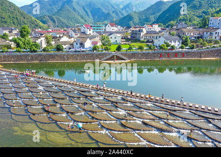 I visitatori un tuffo per rinfrescarsi in acqua in una posizione nota per il pesce in scala barriere sagomati che formano piccole cascate nel quartiere Fuyang, Hangzhou ci Foto Stock