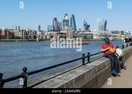 Londra, Inghilterra - 15 Maggio 2018: Un uomo prende una pausa lungo il bordo del fiume Tamigi in una luminosa giornata di sole Foto Stock