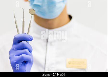 La mano di un maschio di dentista con strumenti su sfondo bianco in clinica. Foto Stock