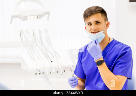 Medico che indossa blu nel suo studio dentistico e guardando la fotocamera con attrezzature mediche sullo sfondo. Foto Stock
