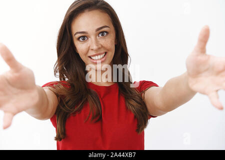 Close-up shot sincera gara femminile donna carina con lentiggini, pulire la pelle, usura t-shirt rossa, tendere le mani avanti, tenere la fotocamera, coccole, dando fr Foto Stock