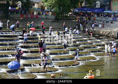 I visitatori un tuffo per rinfrescarsi in acqua in una posizione nota per il pesce in scala barriere sagomati che formano piccole cascate nel quartiere Fuyang, Hangzhou ci Foto Stock