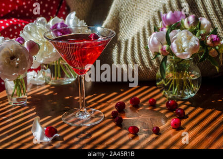 Rustico vita ancora con un bicchiere di rosso a bere con autunno bacche circondato da fiori bianchi su uno sfondo tessile su un tavolo di legno nella diagonale st Foto Stock