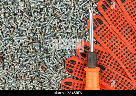 Guanti da lavoro e un cacciavite giacente su un mucchio di viti. Vista superiore Foto Stock