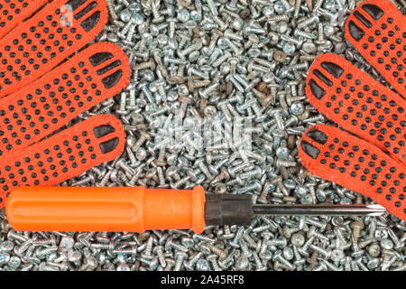 Guanti da lavoro e un cacciavite giacente su un mucchio di viti. Vista superiore Foto Stock