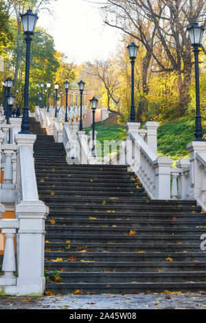 Una scala a chiocciola riempito con caduto foglie d'arancio, circondato da alberi di giallo. Avvolgimento scala di cemento in autunno. Foto Stock