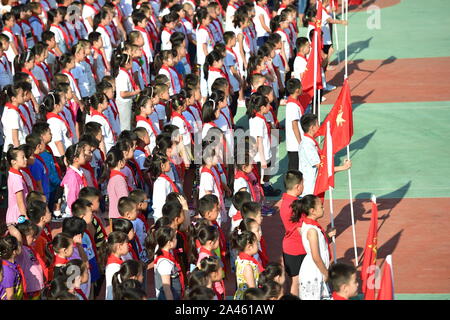 Giovani studenti cinesi che indossa il rosso sciarpe di giovani pionieri della Cina assistere alla cerimonia di apertura per il nuovo semestre presso una scuola primaria in S Foto Stock