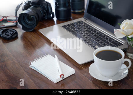 Luogo di lavoro di un fotografo con il computer portatile, fotocamera, lenti tazza di caffè e blocco note su una tavola di legno, spazio copia selezionata, focus, profondità di campo ridotta Foto Stock