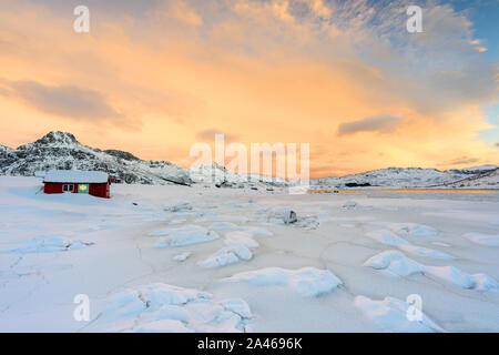 Isole Lofoten in Norvegia e il loro bellissimo paesaggio invernale al tramonto. Idilliaco paesaggio con casa rossa sulla coperta di neve sulla spiaggia. Attrazione turistica Foto Stock