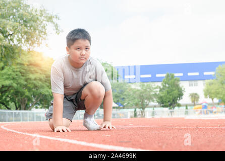 Montare e fiducioso fat boy nella posizione di partenza pronta per l'esecuzione. kid atleta circa per avviare una volata cercando inoltra. concetto di esercizio Foto Stock