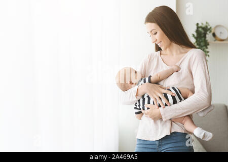 Bella madre millenario tenendo il suo simpatico bimbo sulle mani Foto Stock