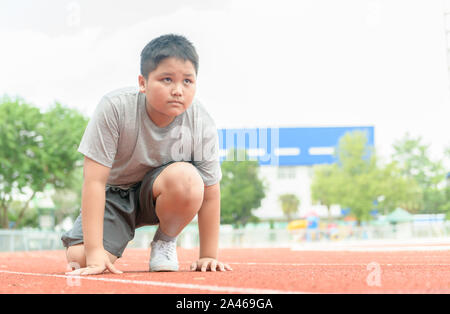 Montare e fiducioso fat boy nella posizione di partenza pronta per l'esecuzione. kid atleta circa per avviare una volata cercando inoltra. concetto di esercizio Foto Stock