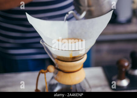 Esperto barista vicino fino a mani preparare deliziosi caffè mentre versando acqua calda nel filtro Foto Stock