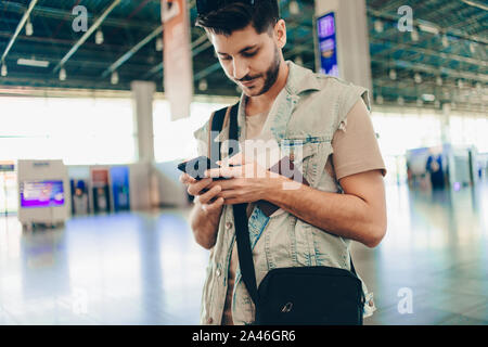 Giovane viaggiatore con passaporto e i biglietti utilizzando il telefono cellulare all'aeroporto Foto Stock