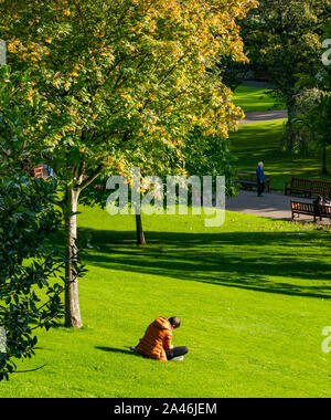 Princes Street Garden, Edimburgo, Scozia, Regno Unito, 12 ottobre 2019. Regno Unito Meteo: persone in Edinburgh godetevi un delizioso caldo autunno soleggiata giornata nella capitale. Un uomo si siede sulla lettura di erba Foto Stock