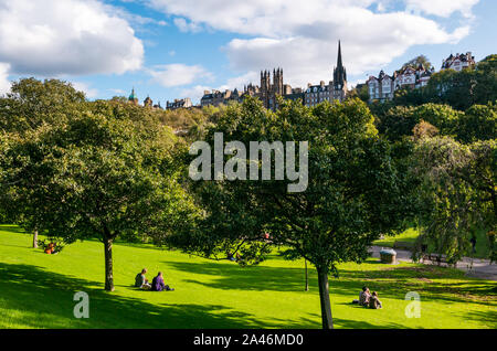 Princes Street Garden, Edimburgo, Scozia, Regno Unito, 12 ottobre 2019. Regno Unito Meteo: persone in Edinburgh godetevi un delizioso caldo autunno soleggiata giornata nella capitale. Persone sedersi sul prato con una vista di Ramsey Gardens Foto Stock