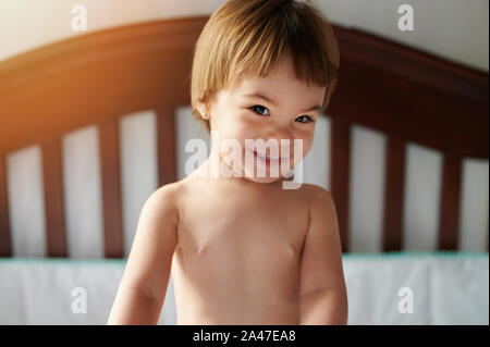 Adorable baby kid sorridente guarda nella telecamera rimanere nel letto Foto Stock