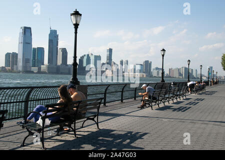 La gente seduta sulle panchine a batteria City Park Esplanade con vista a Jersey City e sul fiume Hudson Foto Stock