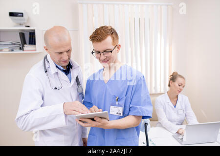 Due medici in uniforme guardando attraverso il documento elettronico sulla schermata del touchpad Foto Stock