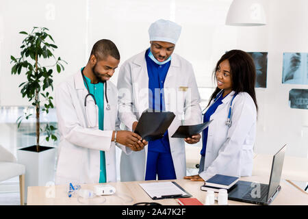 Medici guardando a raggi x in un ospedale. L'uomo africano chirurgo controllo x ray film in ufficio con maschio e femmina medici radiologi residenti Foto Stock