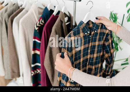 Giovani femmine shopper azienda appendiabiti con camicia a scacchi mentre la scelta di vestiti Foto Stock