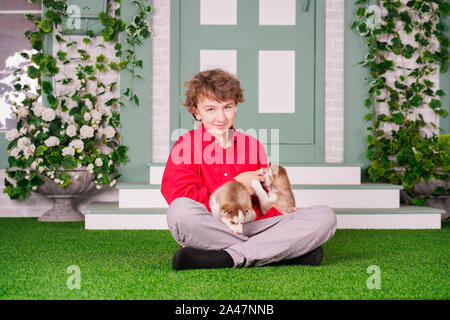 Ragazzo caucasico in maglietta rossa a giocare con due simpatici cuccioli di husky sul prato vicino a casa da solo Foto Stock