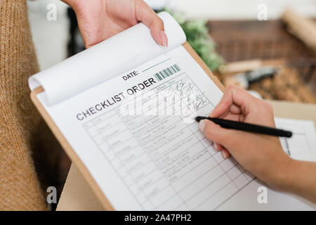 Donna con penna andando a mettere tick di fronte ad uno dei prodotti ordinati in lista Foto Stock