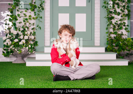 Ragazzo caucasico in maglietta rossa a giocare con due simpatici cuccioli di husky sul prato vicino a casa da solo Foto Stock