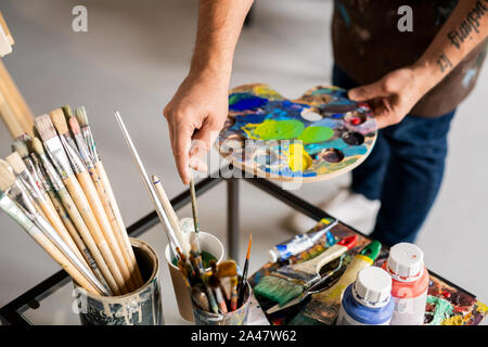 Pittore di contenimento con tavolozza di colori misti e mettendo il pennello in acqua Foto Stock