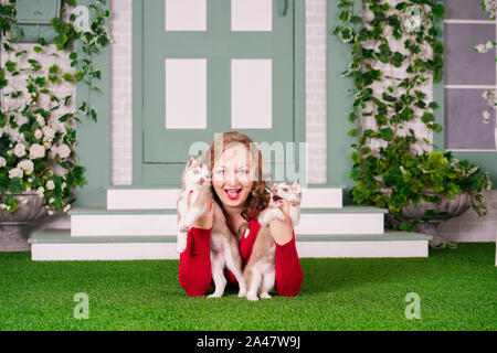 Piuttosto caucasica dimensioni plus woman in red felpa con due simpatici cuccioli di husky su erba verde da solo Foto Stock