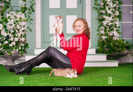 Piuttosto caucasica dimensioni plus woman in red felpa con due simpatici cuccioli di husky su erba verde da solo Foto Stock