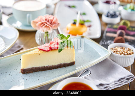 Pezzo di deliziose cheesecake con fragola e foglie di menta sulla piastra bianca. La colazione al caffè, caffè del mattino. Il cappuccino e un sacco di dessert Foto Stock