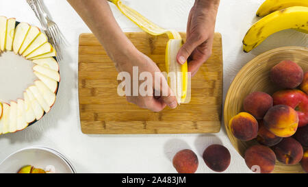 Fette di Banana su un tagliere di legno. Donna Peeling e affettare le banane. Disponendo Frutta Foto Stock