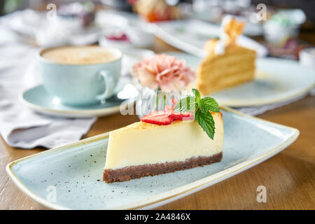 Pezzo di deliziose cheesecake con fragola e foglie di menta sulla piastra bianca. La colazione al caffè, caffè del mattino. Il cappuccino e un sacco di dessert Foto Stock