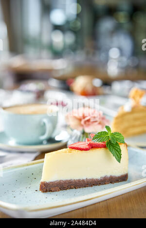 Pezzo di deliziose cheesecake con fragola e foglie di menta sulla piastra bianca. La colazione al caffè, caffè del mattino. Il cappuccino e un sacco di dessert Foto Stock