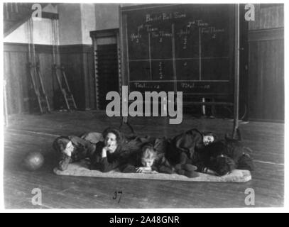 Cinque ragazze giacente sul tappeto in palestra nella parte anteriore del quadro di valutazione di pallacanestro, Western High School di Washington, D.C. Foto Stock