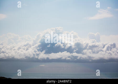 La luce del sole forma un arco blu pallido sotto le nuvole cumulonimbus sospese sull'oceano Foto Stock