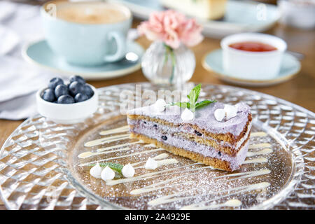 Mirtillo pan di spagna decorata con meringa e le foglie di menta. La colazione al caffè, caffè del mattino. Il cappuccino e un sacco di dolci sul tavolo. Foto Stock