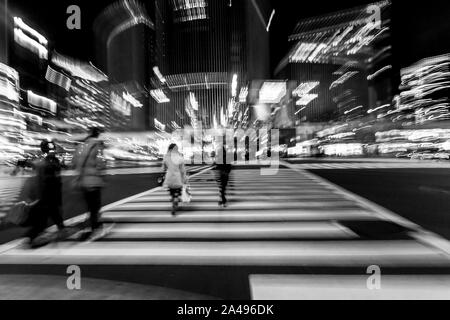 Pedoni che attraversano la strada nel cuore del quartiere di Ginza a Tokyo. Ginza attraversando la notte. Moto sfocata. Foto Stock