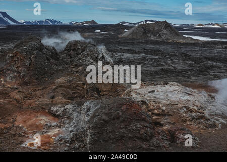 Leirhnjukur vecchio nero e rosso campo di lava con pietre colorate e il fumo proveniente da terra e cielo blu in Islanda, nuvoloso giorno in estate , film effe Foto Stock