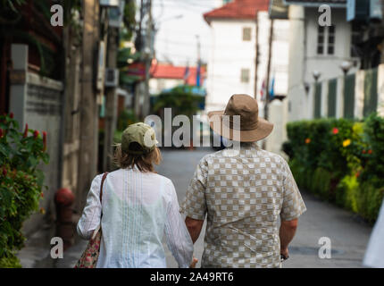 Vista posteriore di ben vestito senior giovane di età compresa tra uomo e donna in cappelli camminando a braccetto in città. Foto Stock