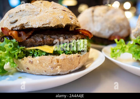 Appetitosi hamburger di manzo, formaggio, lattuga e pancetta fritta su una piastra, tra l'altro cheeseburger. Close-up. Foto Stock
